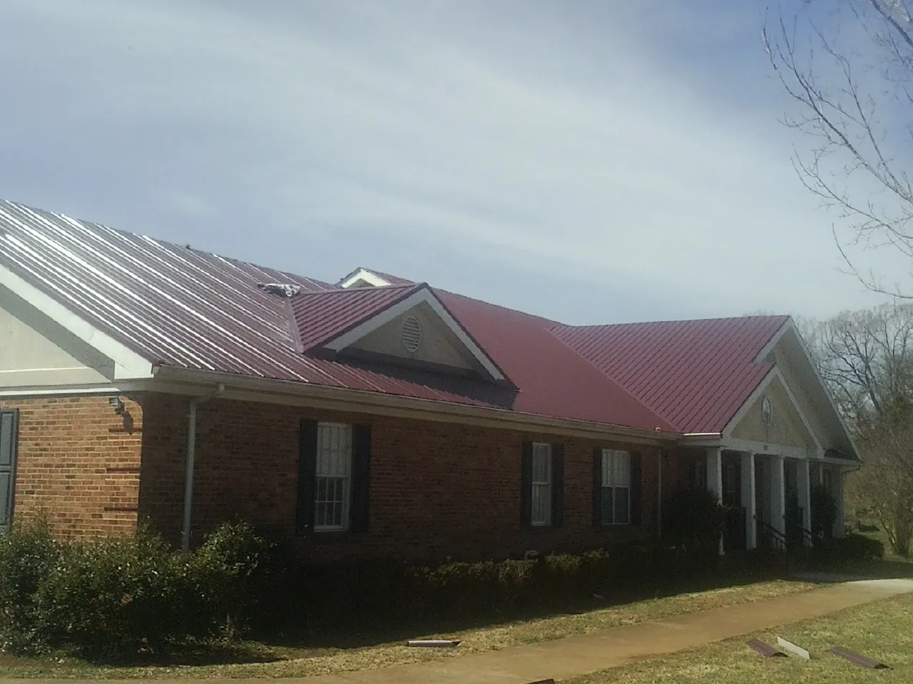 Red metal roof with gabled entries on a long brick building, from a Hail Damage Roof Repair job in New Glarus