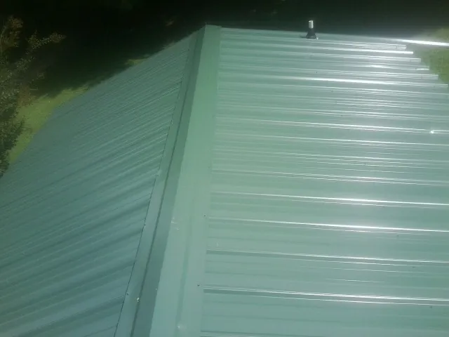 New green metal panels meeting at the ridge of a roof — Flat Roof Repair work by our crew in New Glarus