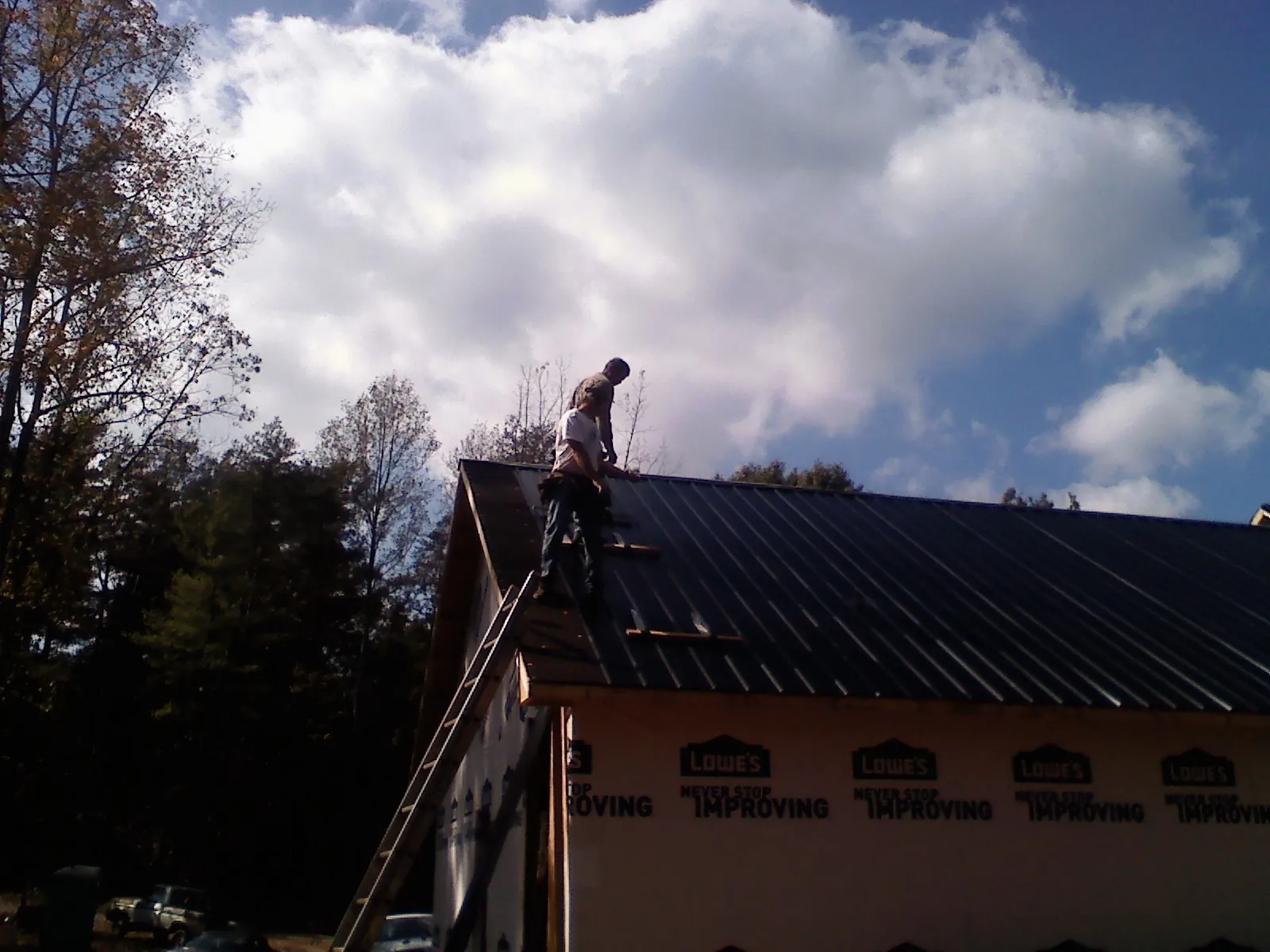 Roofer fastening dark metal panels high against a cloudy sky, from a Roof Inspection job in New Glarus