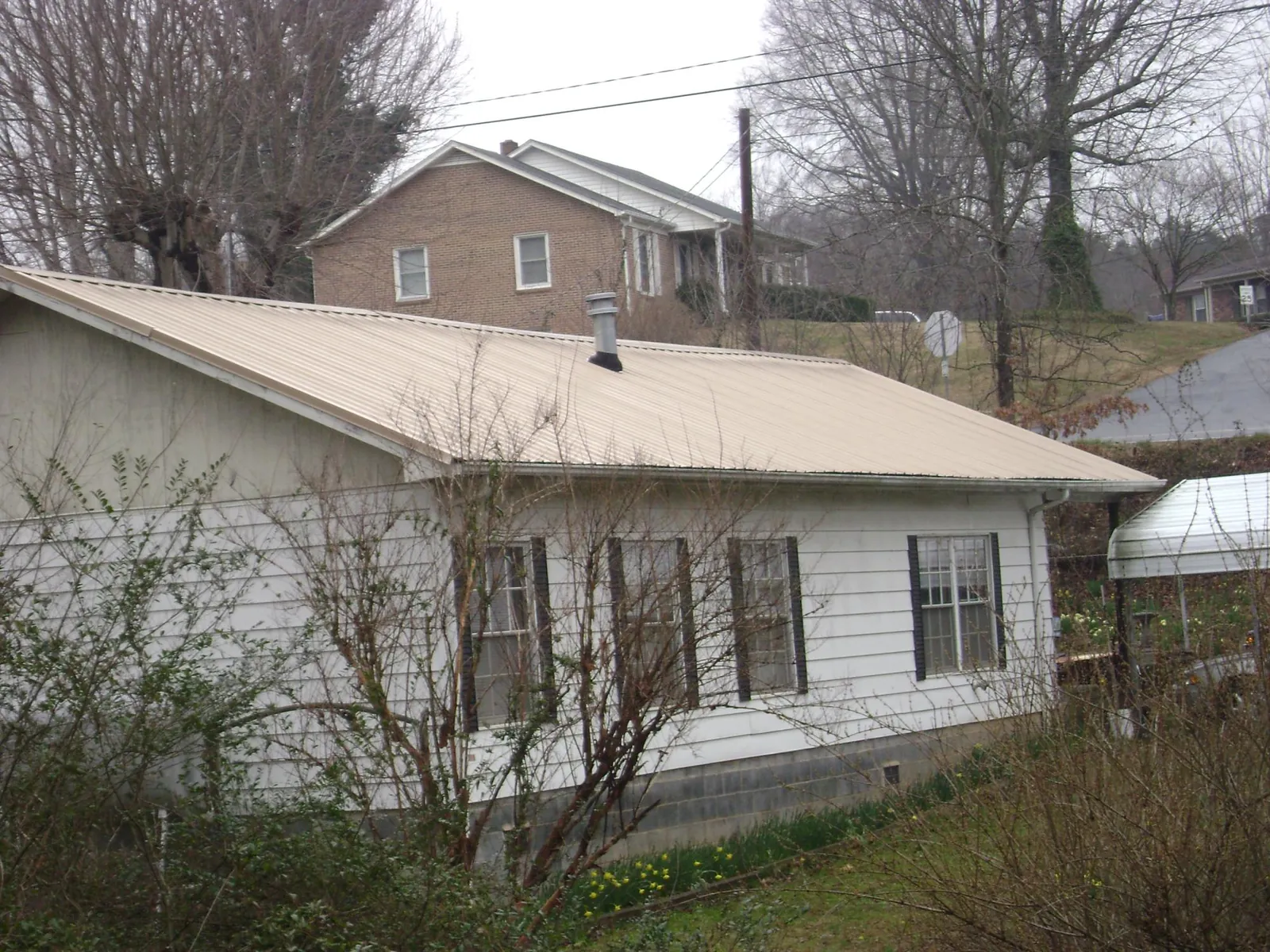 Tan metal roof on a white sided house set into a hillside in New Glarus